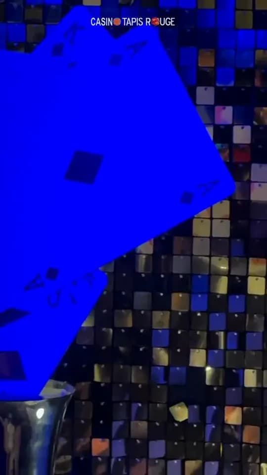 De grandes cartes à jouer bleues devant un mur de paillettes, décor d’une soirée casino